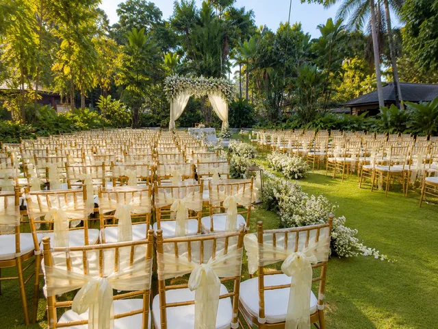 Gold Chiavari chairs for a garden wedding ceremony with white aisle flowers and outdoor arch