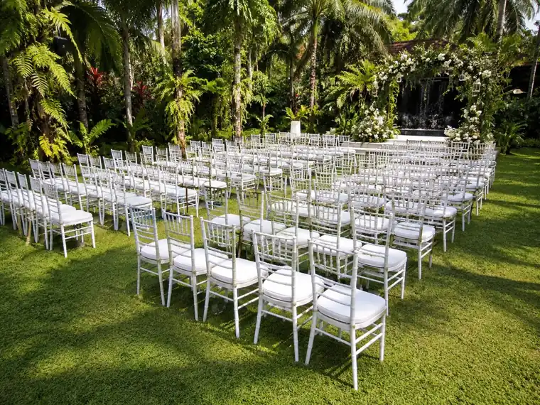 White Chiavari chairs arranged on a garden lawn for an outdoor wedding ceremony