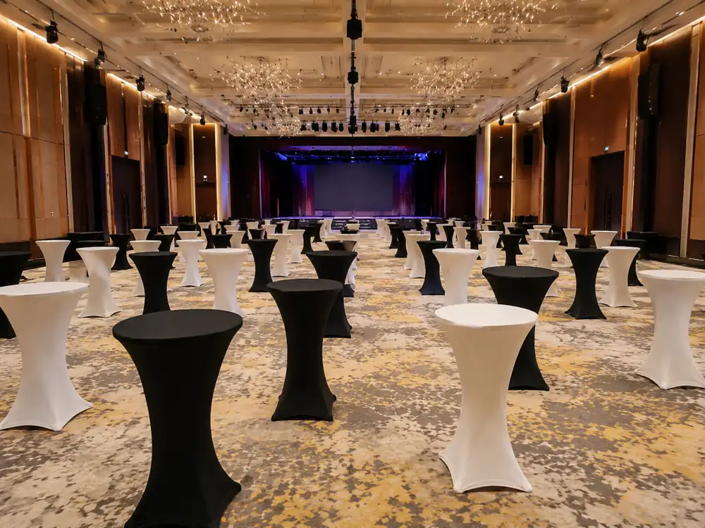 Black and white cocktail tables arranged across a ballroom facing a stage