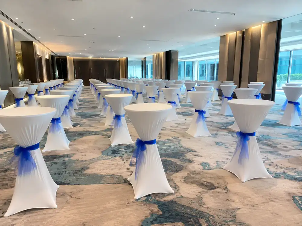 White cocktail tables with blue sash in a bright ballroom setup