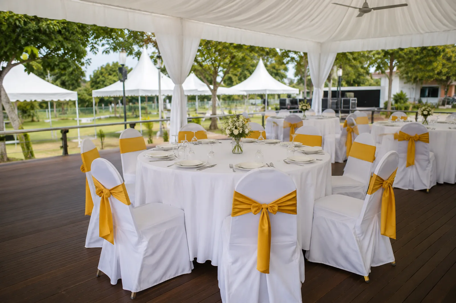 Covered outdoor round table setup with white table cloth and gold sash chairs