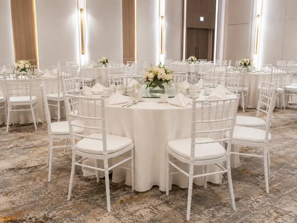 White Tiffany chairs around round banquet tables in a bright event hall
